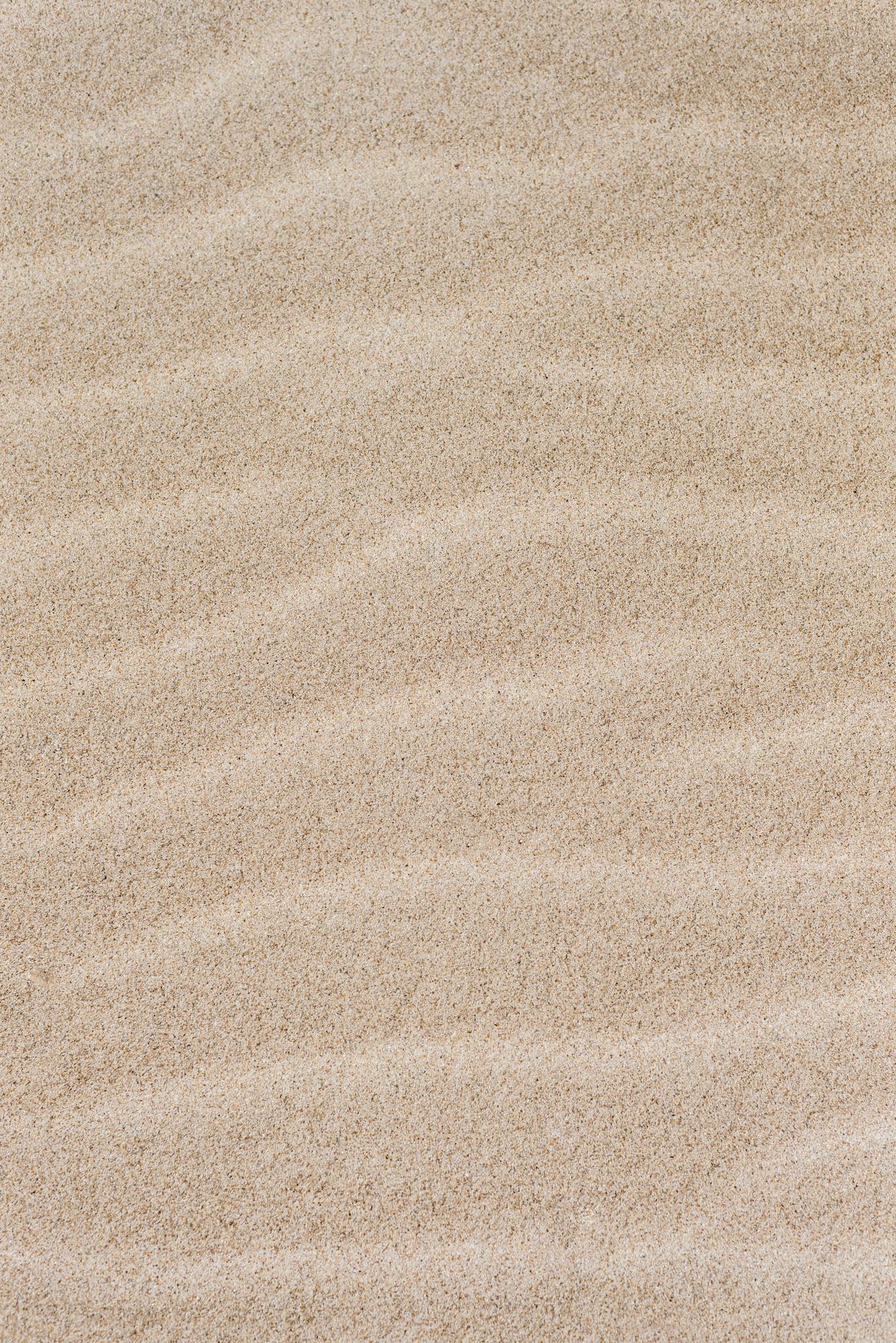 Close-up of sand with natural wave patterns, offering a minimalist and serene texture.