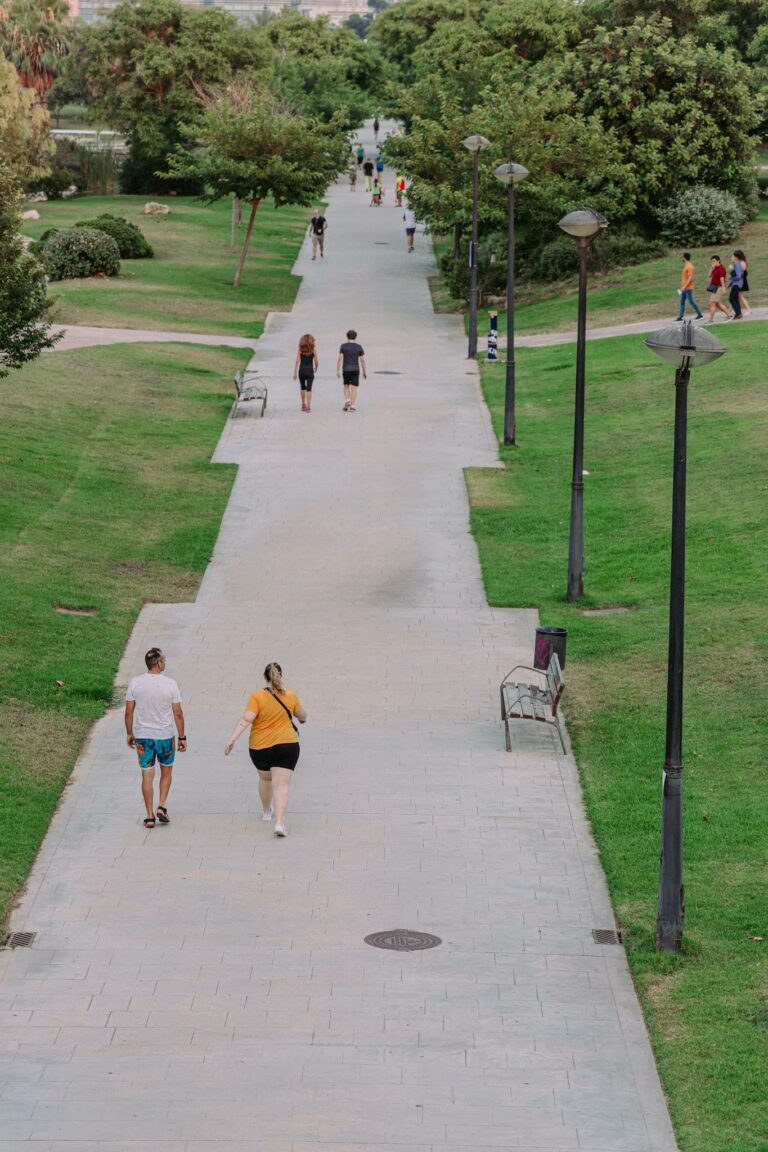 People enjoying a summer walk in a Valencia park with lush greenery.